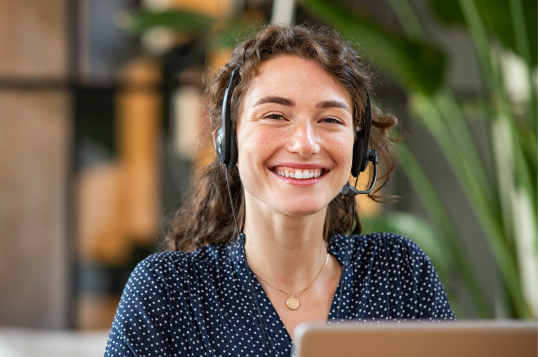 Customer Service Lady smiling, wearing headphones behind a laptop